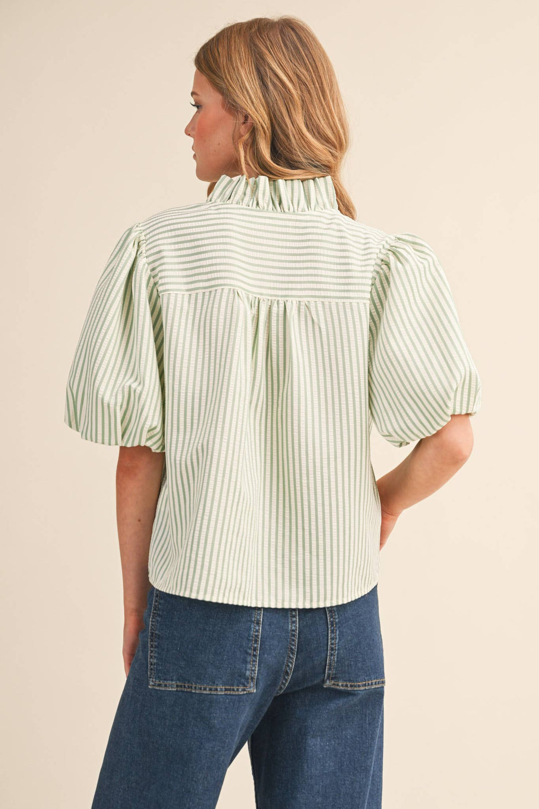 Woman wearing a green and white striped blouse with puffed sleeves on a beige background