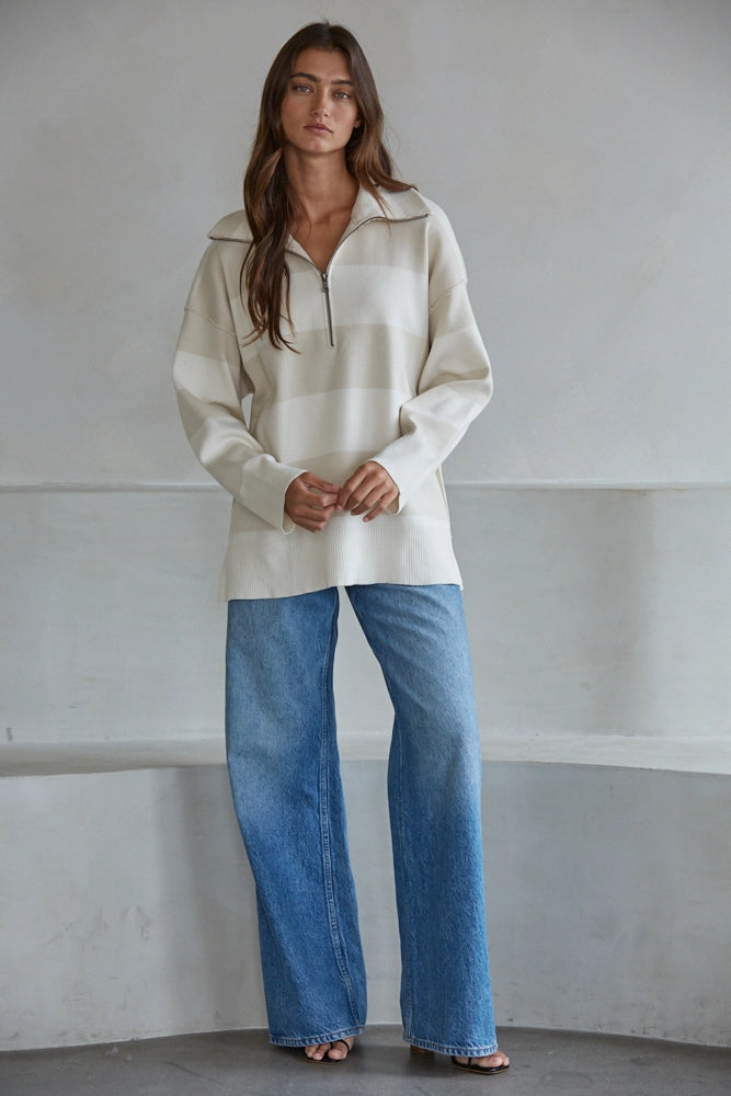 Woman wearing a beige long-sleeve shirt and blue jeans against a plain background