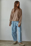 Person wearing a brown sweater and light blue jeans against a plain background
