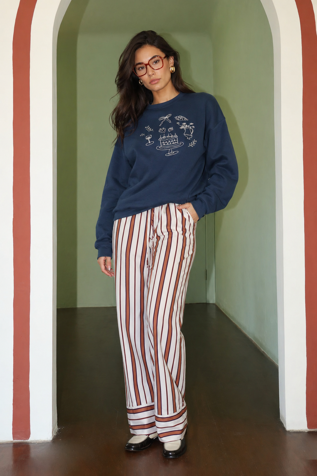 Woman wearing a blue sweater and striped pants standing in a room with colorful walls.