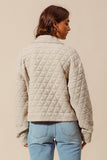 Person wearing a beige quilted jacket and blue jeans on a beige background