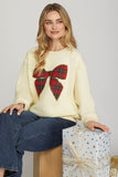 Woman wearing a cream sweater with a red tartan bow design, sitting next to gift boxes.