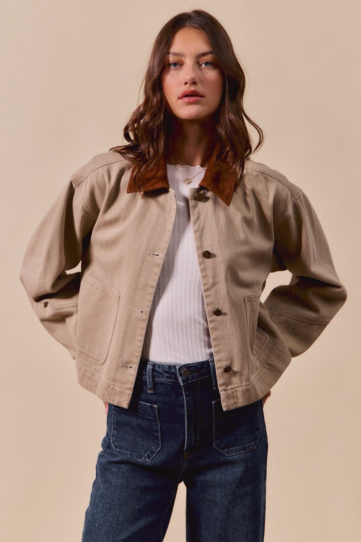 Woman wearing a beige jacket over a white shirt and blue jeans on a beige background