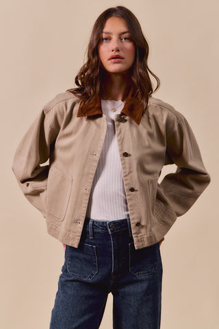 Woman wearing a beige jacket over a white shirt and blue jeans on a beige background
