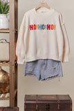 Beige sweater with 'HO HO HO!' text and denim shorts on a hanger against a neutral background.