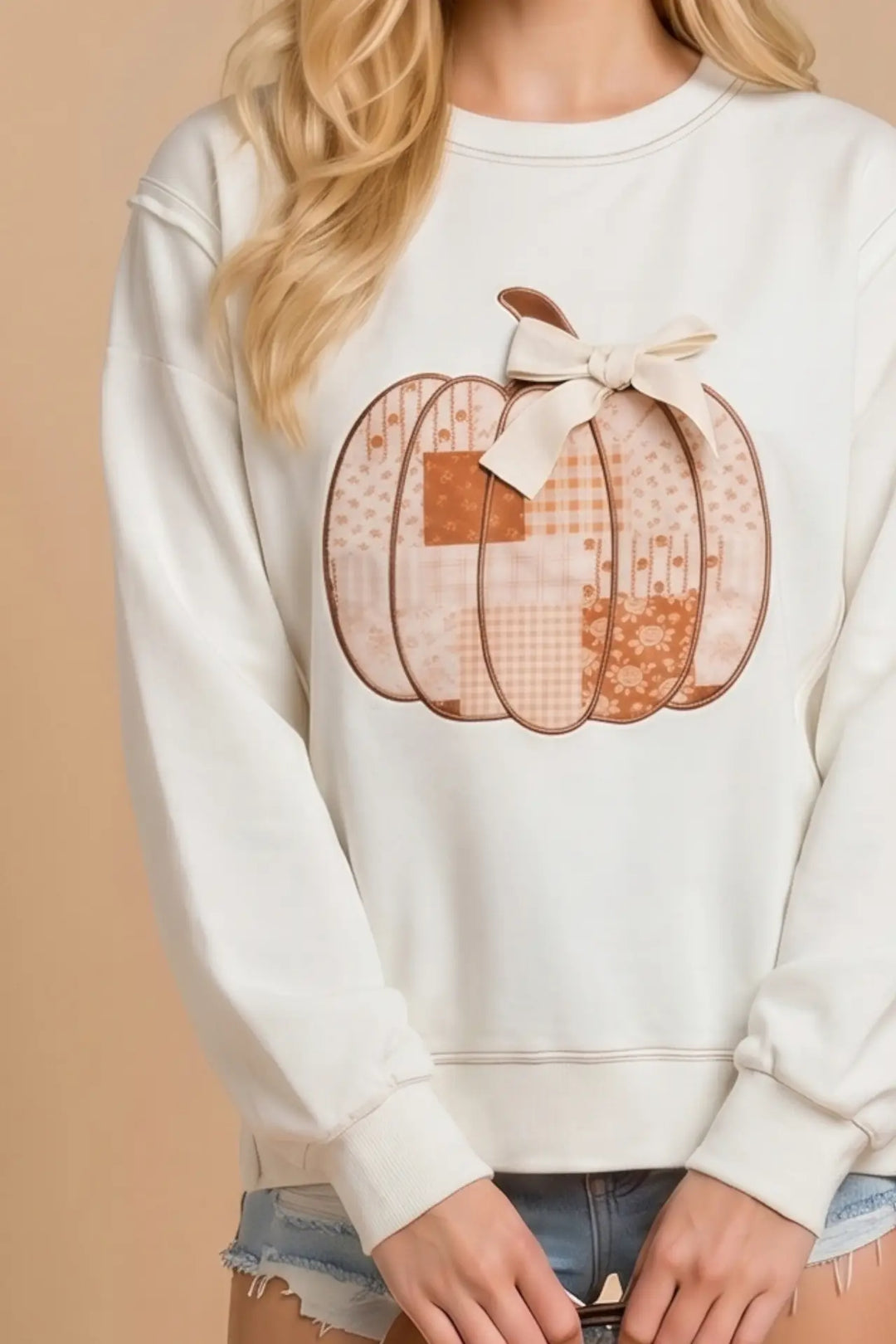 White sweatshirt with a plaid pumpkin graphic worn by a person against a beige background