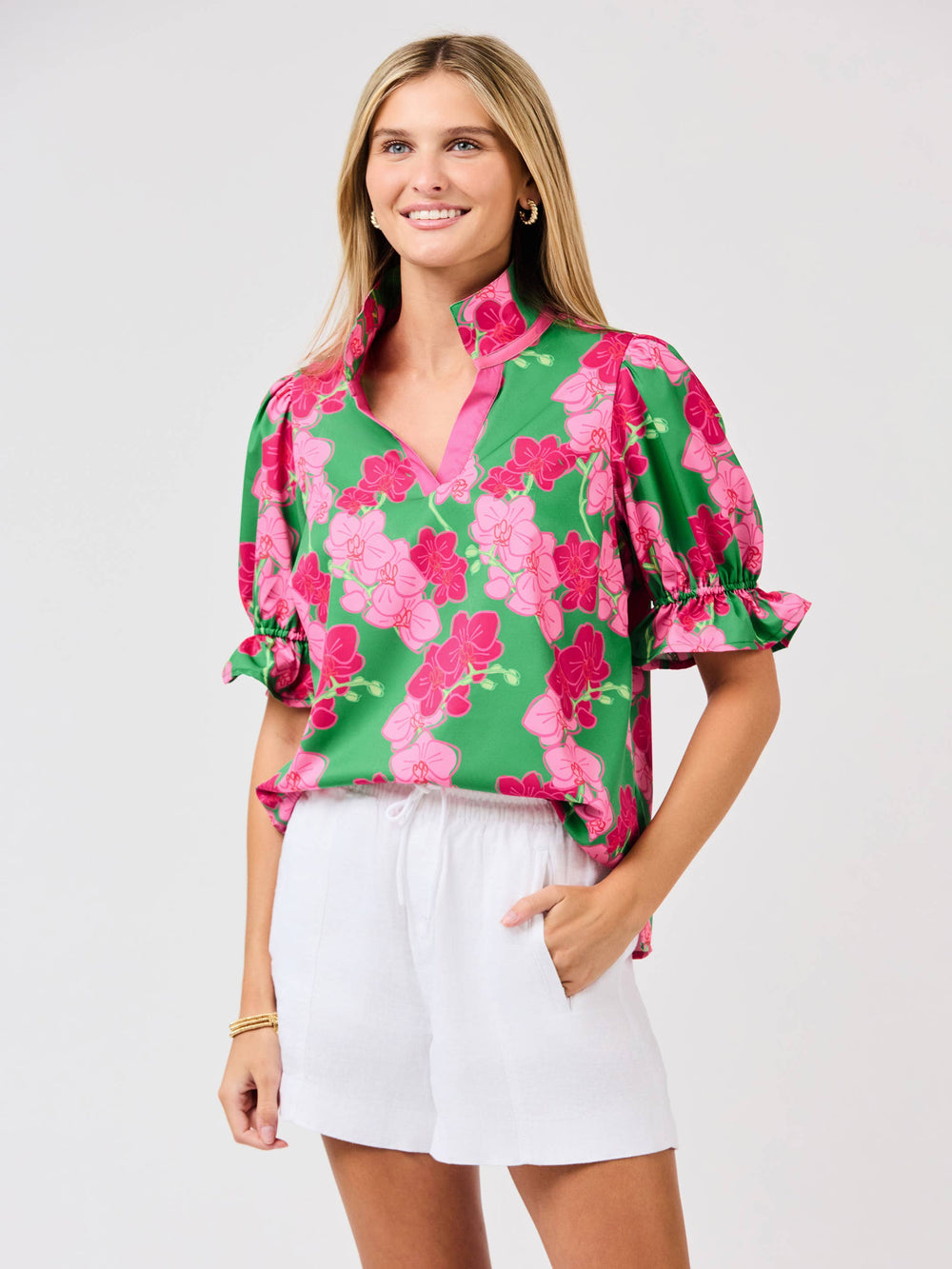 Woman wearing a green floral blouse with white shorts on a light gray background