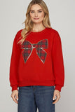 Woman wearing a red sweater with a plaid bow design on a plain background