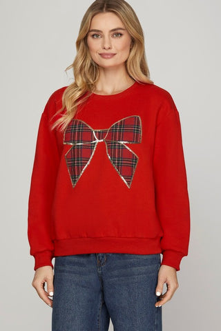 Woman wearing a red sweater with a plaid bow design on a plain background