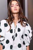 Woman wearing a white blouse with black polka dots against a neutral background