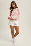 Woman wearing a pink sweater with lace details and white shorts on a plain background