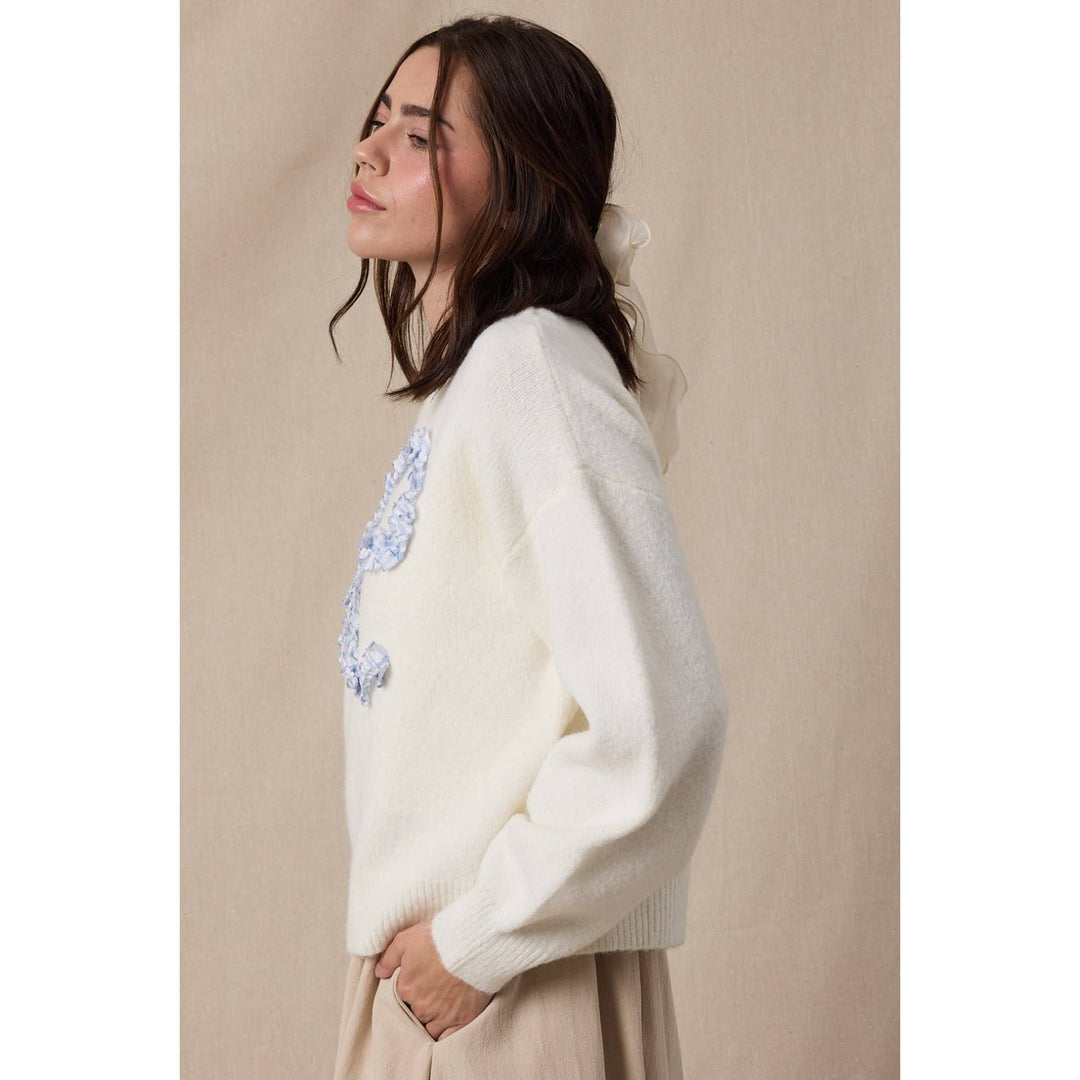 Woman wearing a white sweater with floral embroidery against a beige background