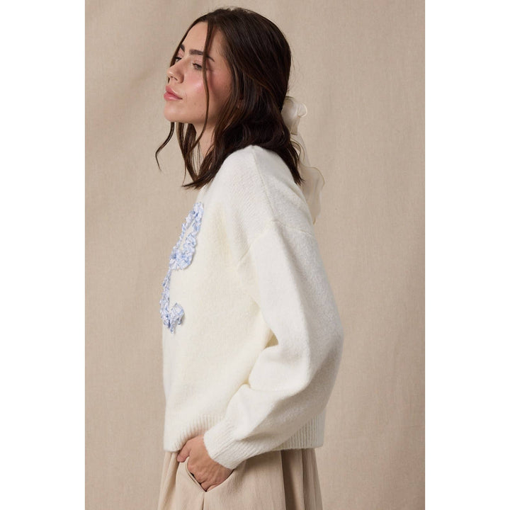 Woman wearing a white sweater with floral embroidery against a beige background