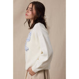 Woman wearing a white sweater with floral embroidery against a beige background