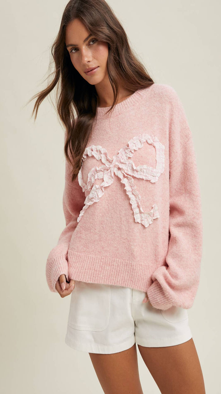 Woman wearing a pink sweater with a lace bow design on a plain background