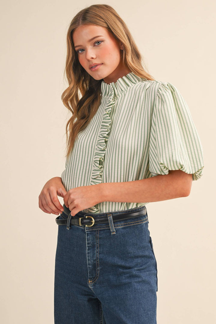 Woman wearing a green and white striped blouse with blue jeans on a beige background
