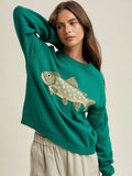 Woman wearing a teal sweater with a fish design on a beige background