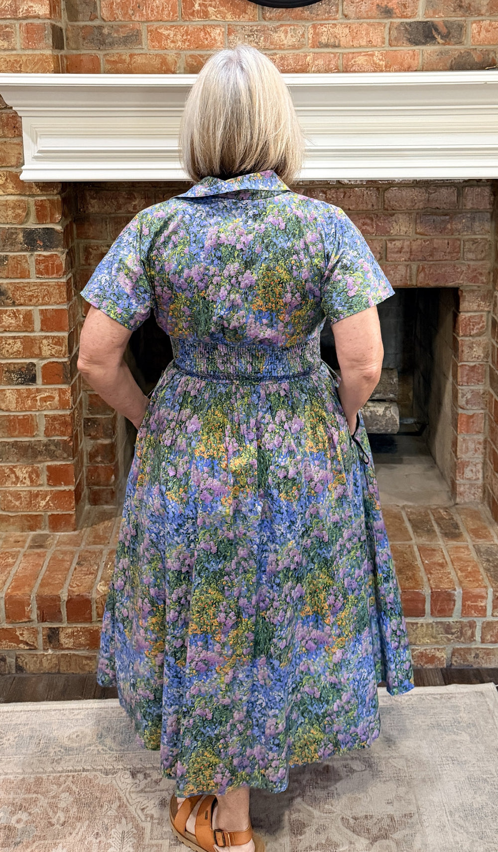 Person wearing a floral dress standing in front of a brick fireplace.