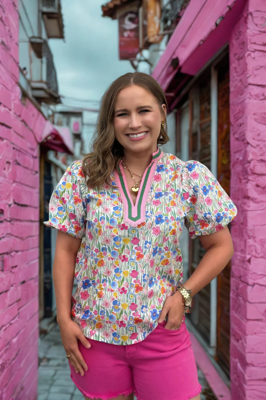 Woman wearing a colorful floral blouse and pink shorts standing in front of pink walls.