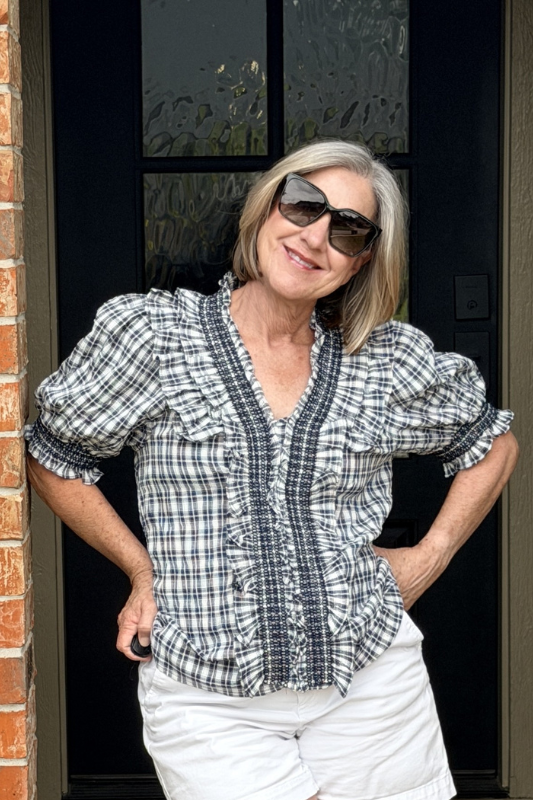 Woman wearing sunglasses and a checkered shirt standing in front of a door.