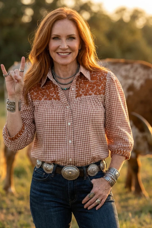 Woman in a plaid shirt and jeans standing in a field with a cow in the background