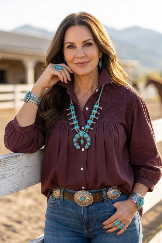 Woman wearing a burgundy shirt, turquoise jewelry, and blue jeans outdoors.
