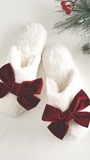 White slippers with red velvet bows on a light background