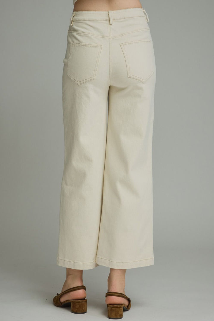 A person shown from the back wearing off-white cropped wide-leg pants and brown heeled sandals against a plain light gray studio background.