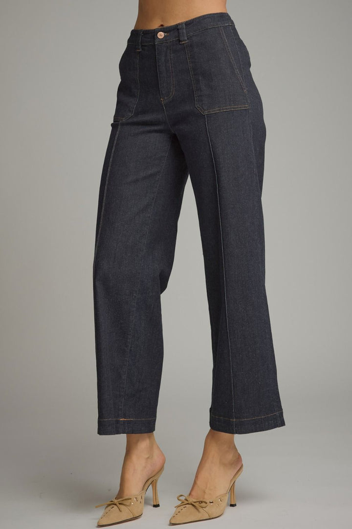 Dark wash cropped denim pants shown on a model from the waist down, paired with beige pointed-toe mule heels against a neutral gray studio background.