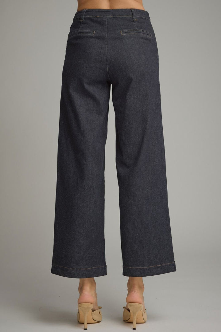 Rear view of a person wearing dark indigo wide-leg cropped jeans with beige mule heels, shown against a plain light gray studio background.