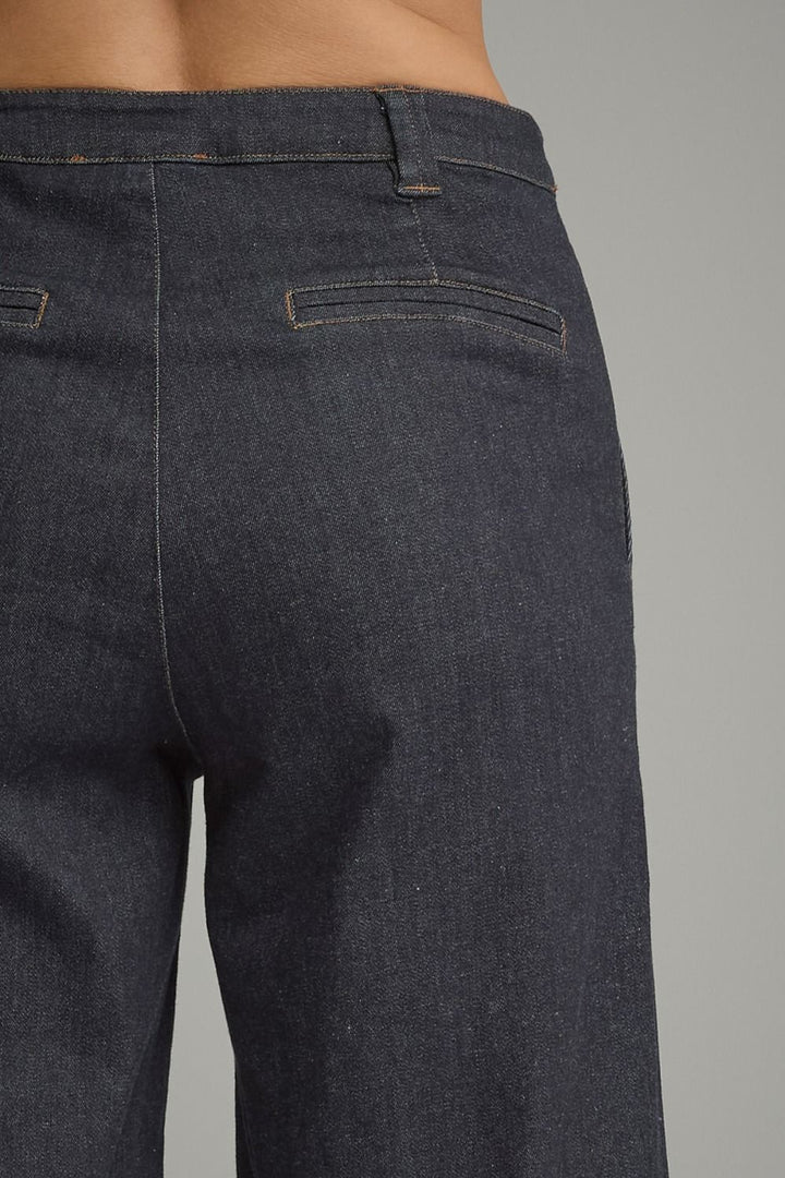 Close-up back view of a person wearing dark indigo denim jeans, showing the waistband, belt loops, back pockets, and fabric texture against a plain gray background.