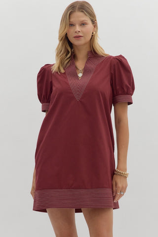 Woman wearing a burgundy dress with puff sleeves on a plain background