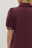 Burgundy blouse with leopard print cuffs on a plain background