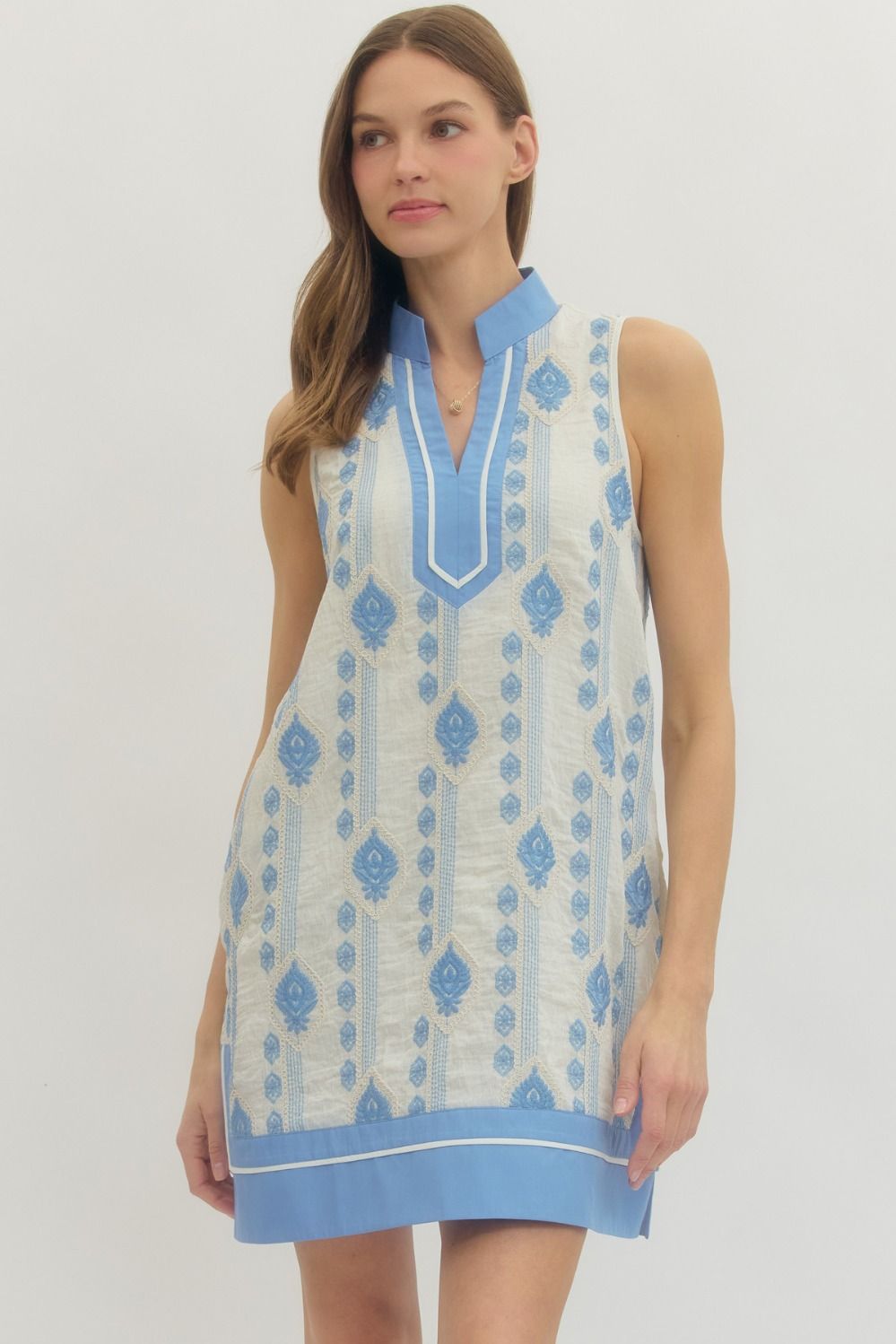 Woman wearing a sleeveless dress with blue and white pattern on a plain background