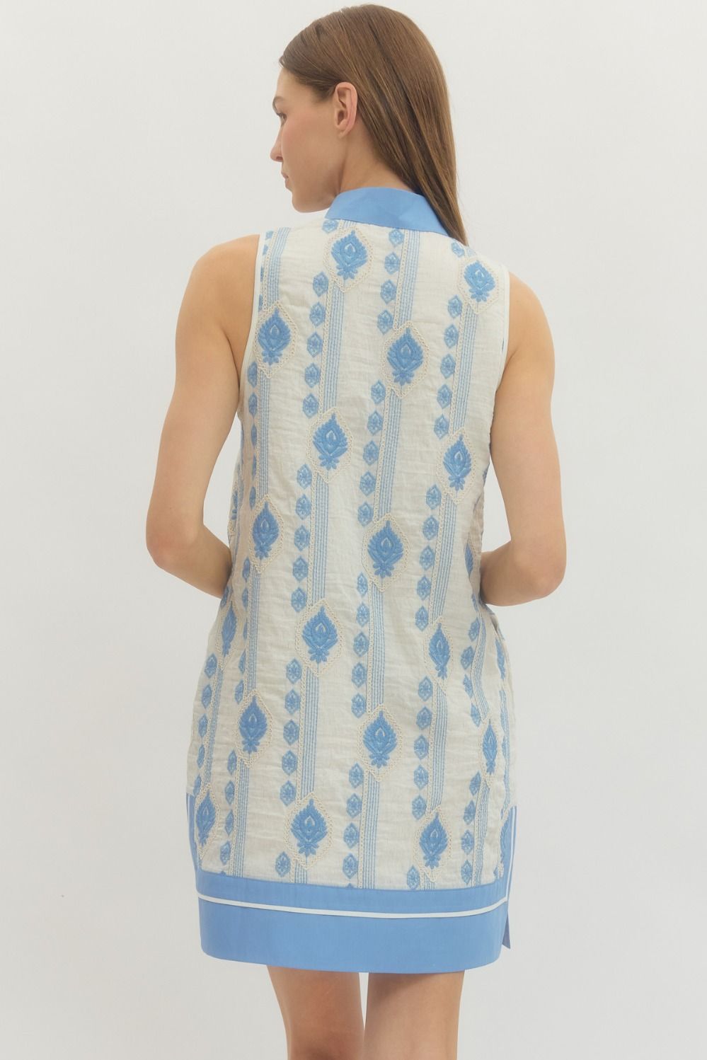 Woman wearing a sleeveless dress with blue and white pattern on a plain background