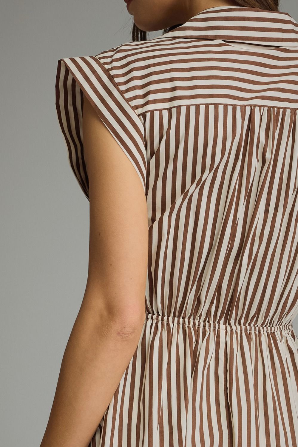 Close-up back view of a person wearing a sleeveless dress with vertical brown and cream stripes and a gathered waist.