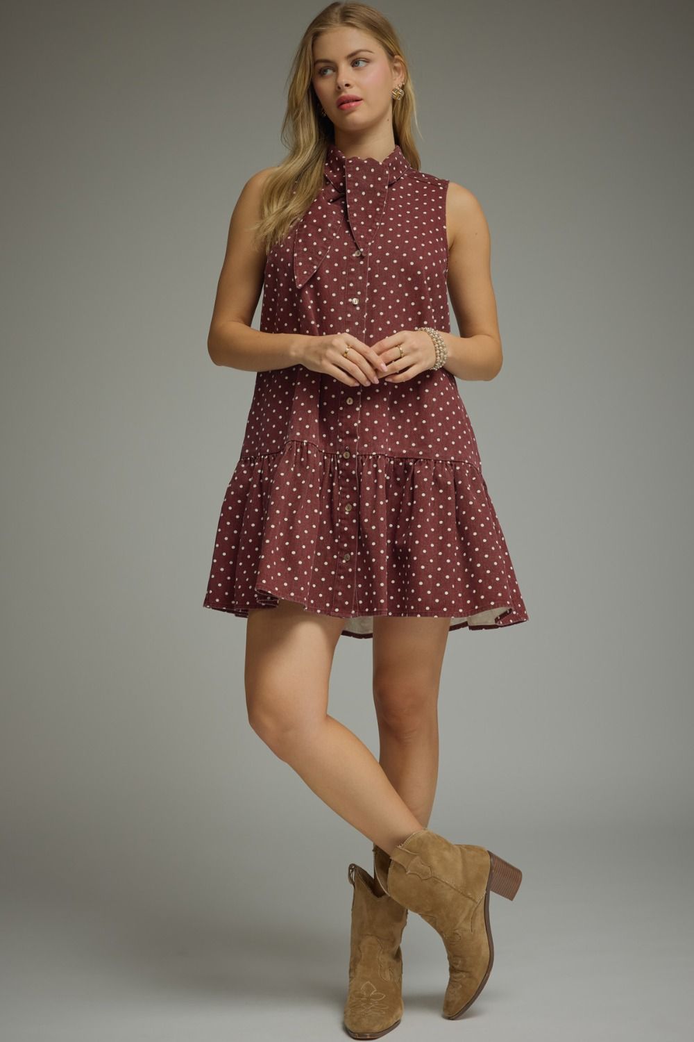Woman wearing a maroon dress with white polka dots and brown boots on a gray background