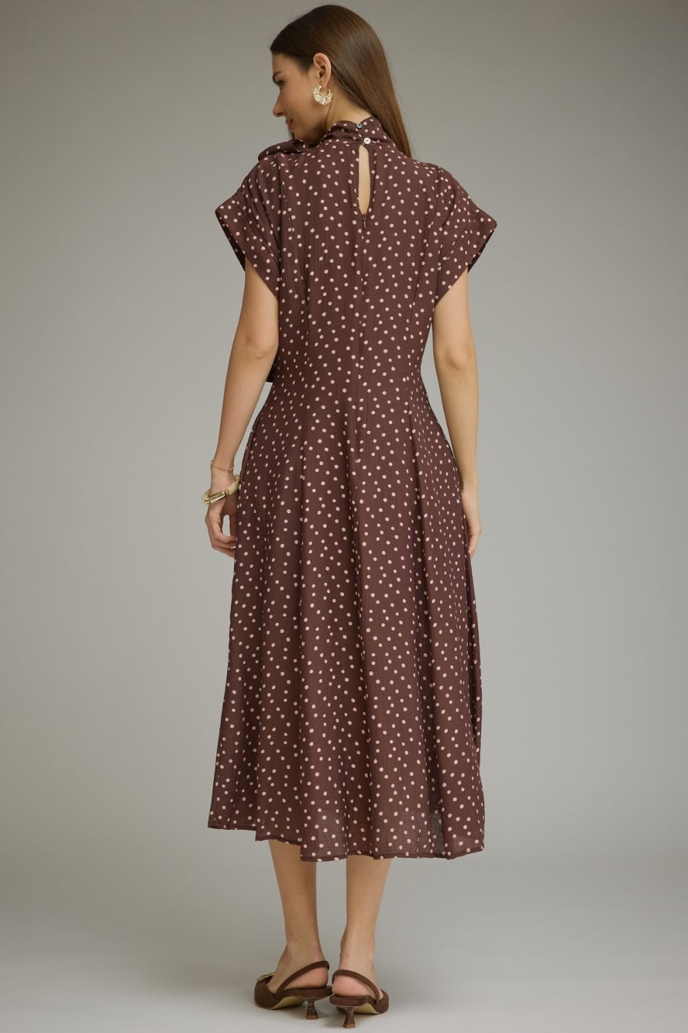 A woman modeling a brown midi dress with a white polka dot pattern, shown from the back against a neutral gray studio background.