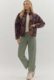 Woman wearing a patterned jacket and green pants on a white background