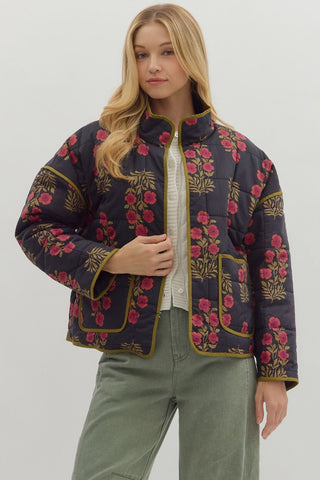Woman wearing a dark floral embroidered jacket on a plain background