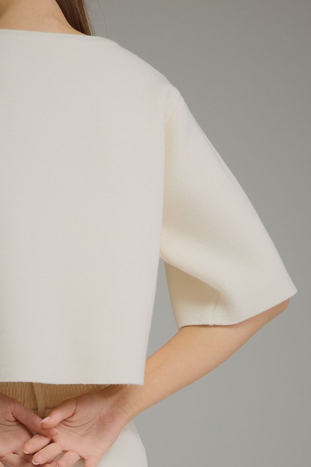 Close-up of a model wearing a cream-colored short-sleeve top or cape-style blouse against a plain gray studio background.
