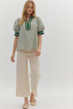 Woman wearing a green and white striped blouse with a high collar and beige pants on a white background