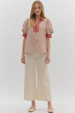 Woman wearing a striped blouse with red accents and beige pants on a white background