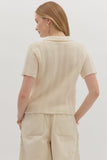 Woman wearing a beige knitted top and pants against a plain background