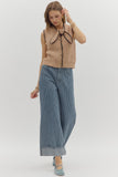 Woman wearing a beige sleeveless sweater with a bow and blue striped pants on a white background