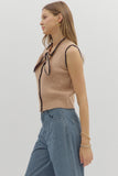 Woman wearing a beige sleeveless top with black trim and blue striped pants on a light gray background