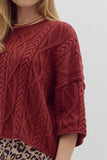 Red knitted sweater with cable pattern worn by a person on a light gray background