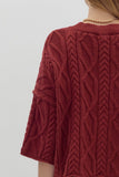 Red cable knit sweater worn by a person on a light gray background