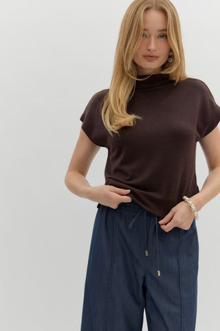 Woman wearing a brown turtleneck and navy pants on a white background