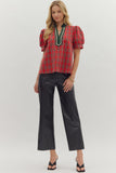 Woman wearing a red plaid blouse with green trim and black pants on a white background